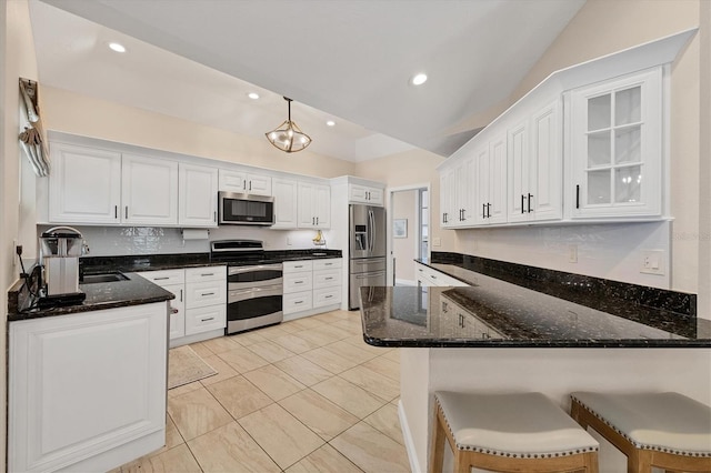 kitchen with vaulted ceiling, white cabinets, a kitchen bar, kitchen peninsula, and stainless steel appliances