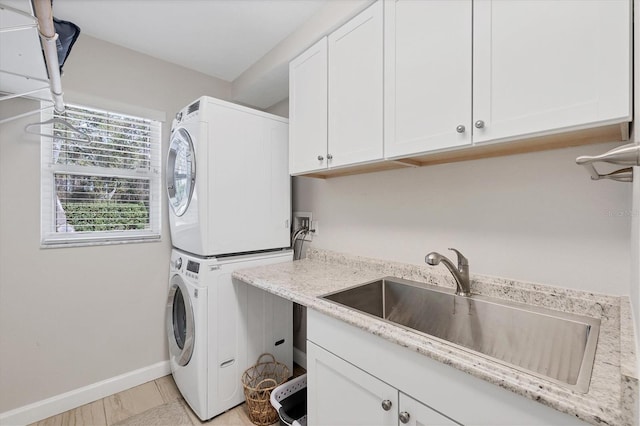 washroom with cabinets, stacked washer and dryer, and sink