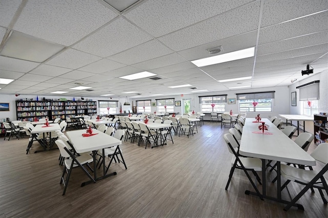 dining area featuring a drop ceiling, wood-type flooring, and plenty of natural light