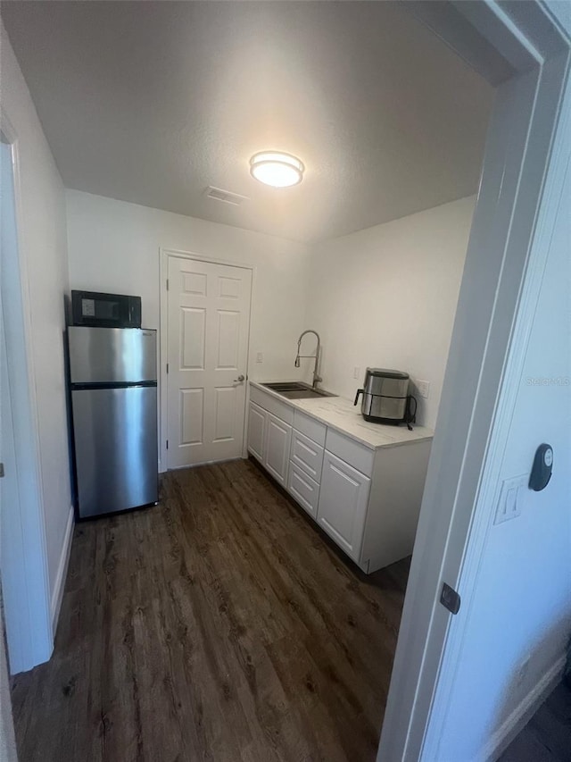 kitchen with dark hardwood / wood-style flooring, sink, stainless steel fridge, and white cabinets