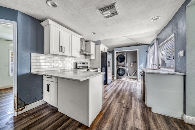 kitchen featuring white cabinetry, stacked washer and dryer, appliances with stainless steel finishes, and wall chimney exhaust hood