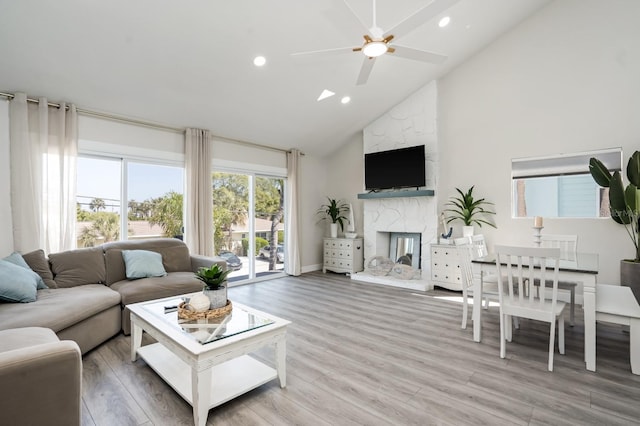 living room featuring ceiling fan, wood-type flooring, a stone fireplace, and high vaulted ceiling