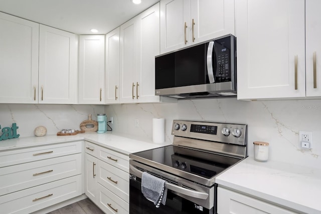 kitchen with electric stove, backsplash, white cabinetry, and light stone countertops