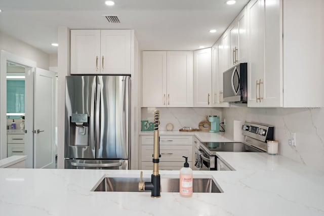 kitchen with sink, white cabinetry, backsplash, stainless steel appliances, and light stone counters