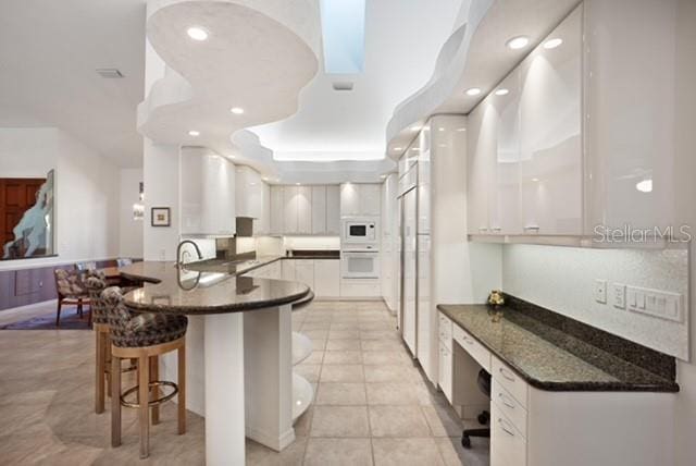 kitchen featuring white cabinetry, sink, light tile patterned floors, and white appliances