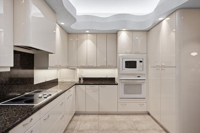 kitchen with white appliances, dark stone countertops, tasteful backsplash, white cabinets, and light tile patterned flooring