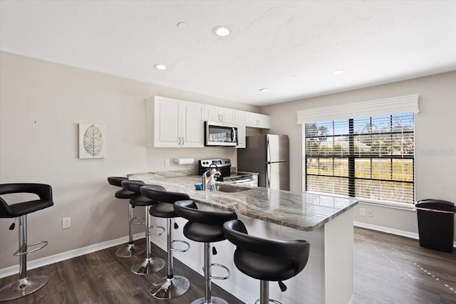 kitchen featuring a breakfast bar, appliances with stainless steel finishes, light stone countertops, white cabinets, and kitchen peninsula