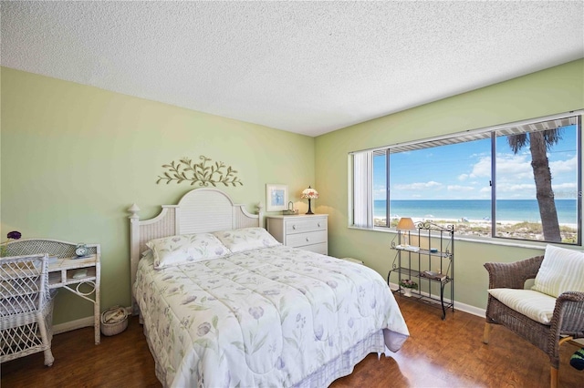 bedroom featuring dark wood-type flooring, a beach view, a textured ceiling, and a water view