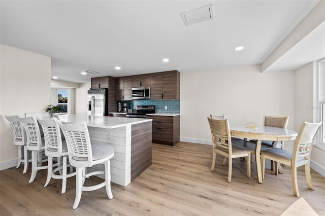 kitchen featuring a kitchen bar, decorative backsplash, light hardwood / wood-style floors, dark brown cabinetry, and stainless steel appliances