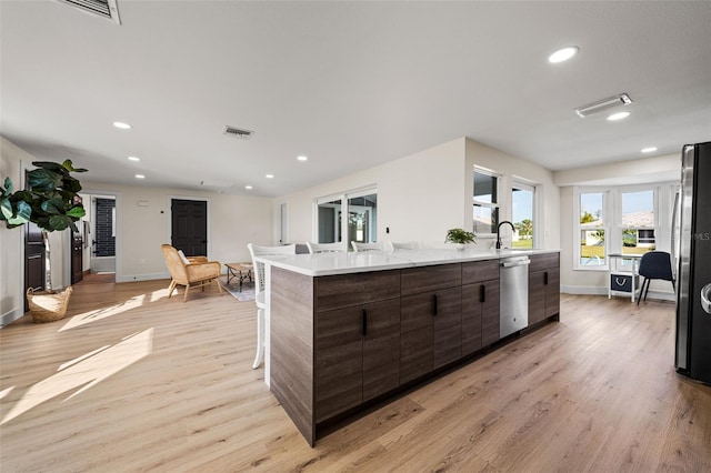 kitchen with sink, appliances with stainless steel finishes, dark brown cabinets, light hardwood / wood-style floors, and a large island with sink