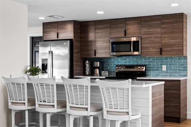 kitchen with appliances with stainless steel finishes, dark brown cabinets, a kitchen bar, and decorative backsplash