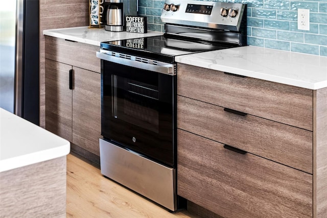 kitchen featuring light stone counters, backsplash, stainless steel appliances, and light wood-type flooring