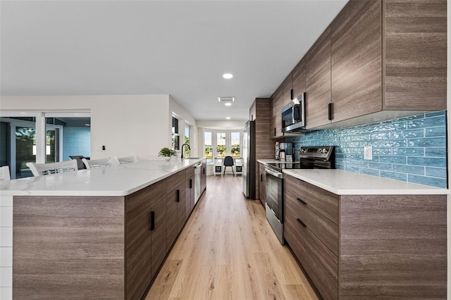 kitchen with appliances with stainless steel finishes, backsplash, a spacious island, a kitchen bar, and light wood-type flooring