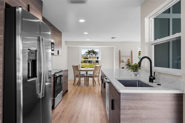 kitchen with stainless steel appliances, dark brown cabinets, sink, and light hardwood / wood-style flooring