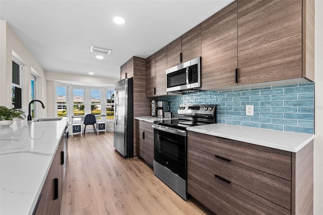 kitchen with sink, backsplash, stainless steel appliances, light stone countertops, and light wood-type flooring