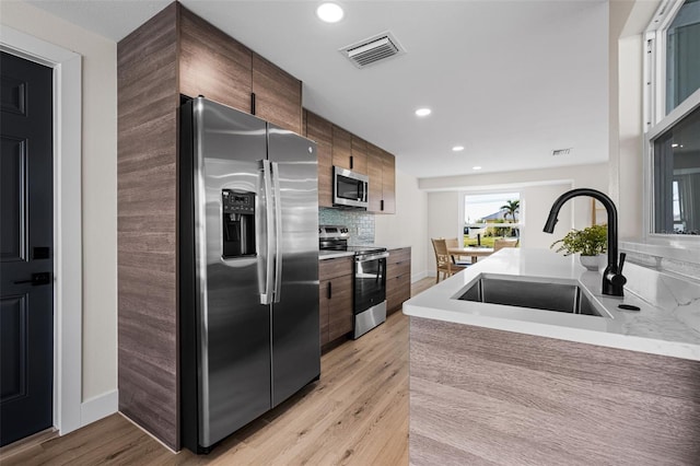 kitchen featuring tasteful backsplash, appliances with stainless steel finishes, sink, and light hardwood / wood-style flooring