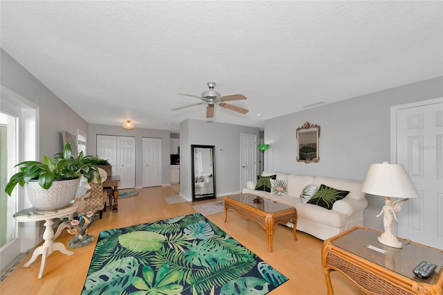 living room featuring ceiling fan, light hardwood / wood-style floors, and a textured ceiling