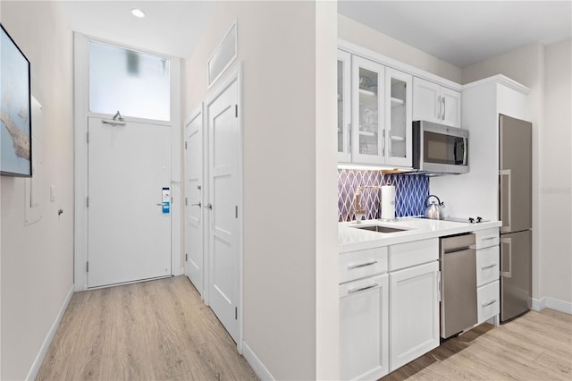 kitchen with sink, backsplash, white cabinets, stainless steel appliances, and light wood-type flooring