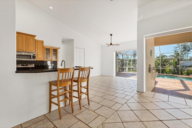 kitchen featuring stainless steel appliances, dark countertops, a ceiling fan, a breakfast bar, and glass insert cabinets