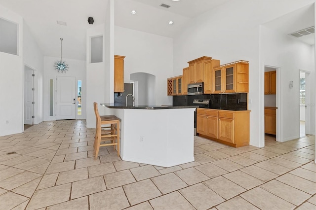 kitchen with stainless steel microwave, high vaulted ceiling, light tile patterned flooring, dark countertops, and backsplash