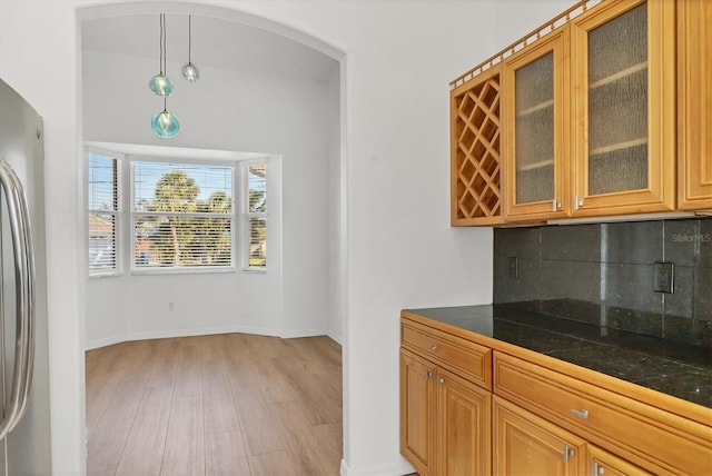 kitchen featuring arched walkways, freestanding refrigerator, light wood-style flooring, decorative backsplash, and glass insert cabinets