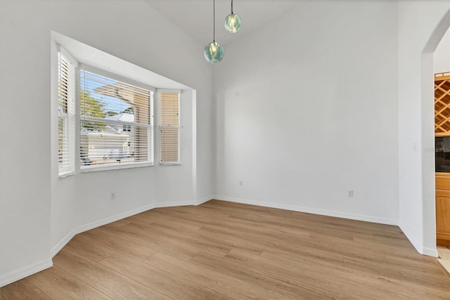 unfurnished dining area with arched walkways, light wood-type flooring, and baseboards