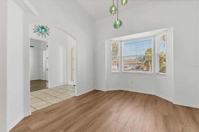spare room featuring light wood finished floors, arched walkways, and baseboards