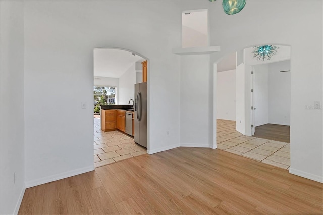 empty room with arched walkways, light wood-type flooring, baseboards, and a high ceiling