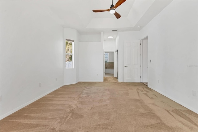 unfurnished bedroom featuring light carpet, a raised ceiling, baseboards, and a ceiling fan