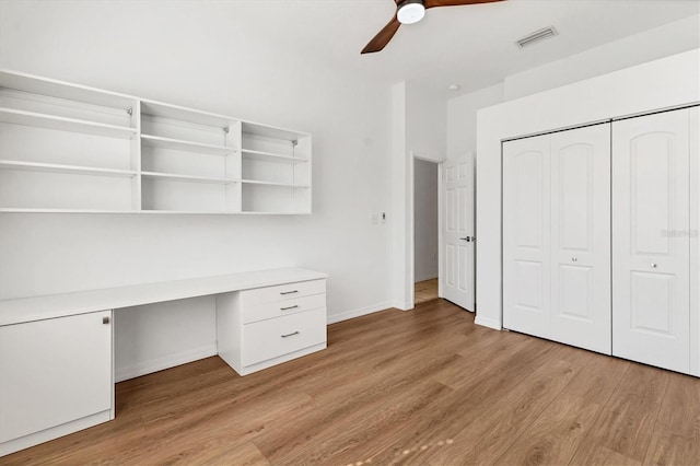 unfurnished office with built in study area, light wood finished floors, a ceiling fan, and baseboards