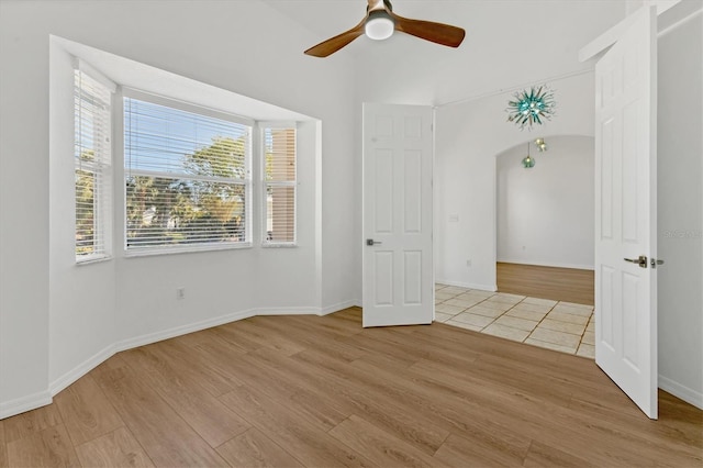 spare room featuring light wood finished floors, a ceiling fan, arched walkways, and baseboards