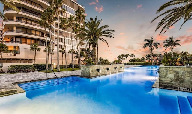 pool at dusk featuring pool water feature