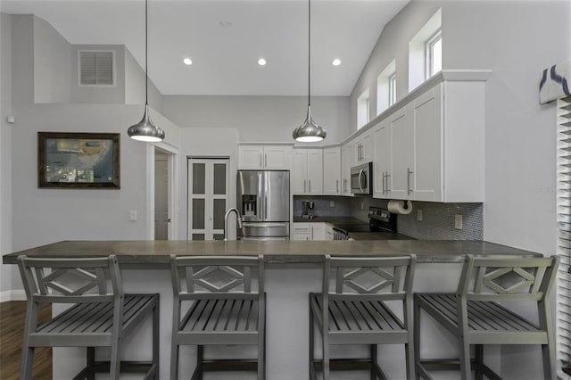 kitchen featuring pendant lighting, stainless steel appliances, white cabinets, a kitchen bar, and kitchen peninsula