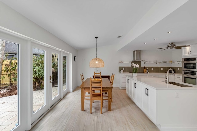 dining room featuring sink, white cabinetry, decorative light fixtures, light wood-type flooring, and a kitchen island with sink