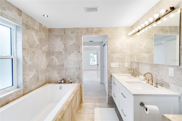 bathroom featuring tiled tub, vanity, and tile walls