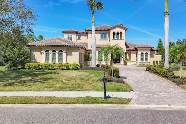 mediterranean / spanish house featuring stucco siding, a front lawn, decorative driveway, and a tiled roof