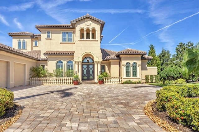 mediterranean / spanish-style house featuring french doors, decorative driveway, a tile roof, and stucco siding