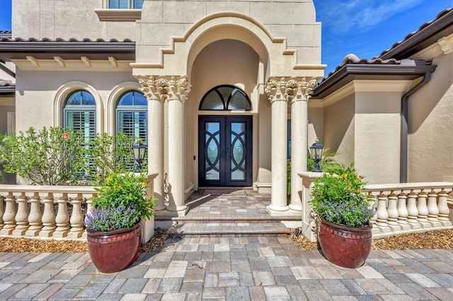 view of exterior entry with french doors, a tile roof, and stucco siding