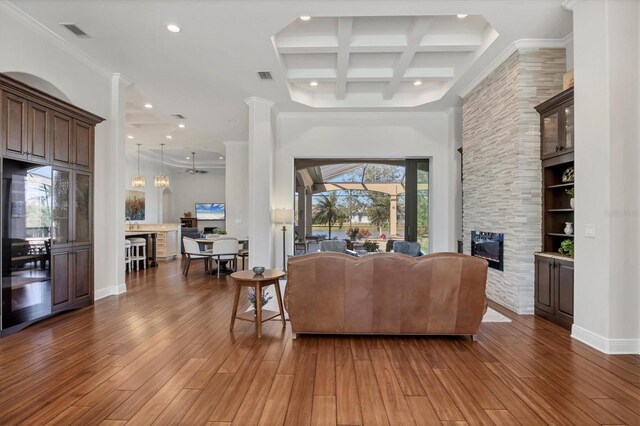 living area with a fireplace, visible vents, coffered ceiling, and wood finished floors