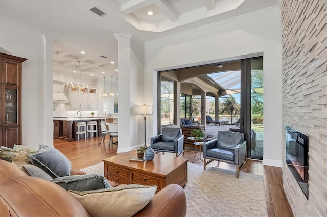 living area featuring visible vents, coffered ceiling, beamed ceiling, wood finished floors, and a stone fireplace