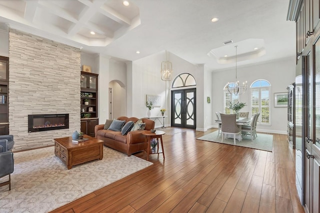 living room with a large fireplace, a high ceiling, coffered ceiling, wood finished floors, and an inviting chandelier