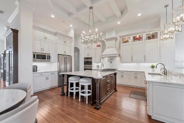 kitchen with arched walkways, coffered ceiling, appliances with stainless steel finishes, wood finished floors, and a sink