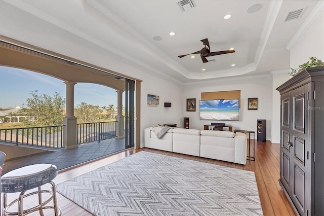 living room featuring light wood finished floors, crown molding, visible vents, and a tray ceiling