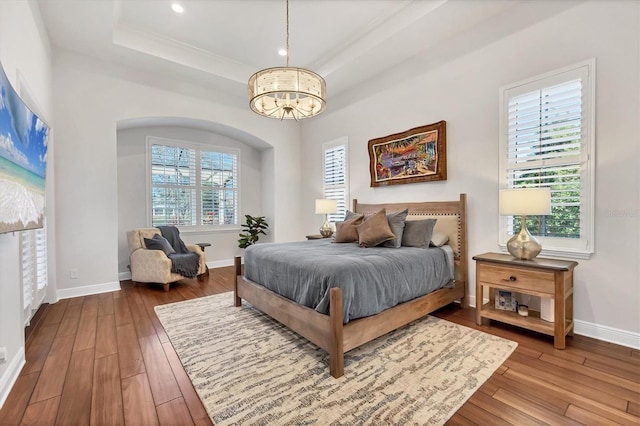 bedroom with baseboards, hardwood / wood-style flooring, a tray ceiling, a notable chandelier, and recessed lighting