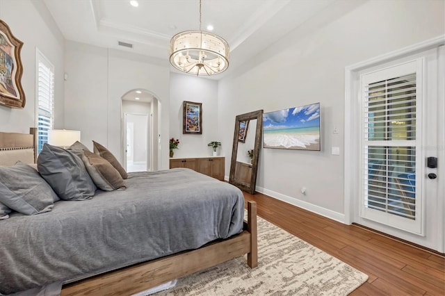 bedroom with arched walkways, wood finished floors, visible vents, baseboards, and a raised ceiling