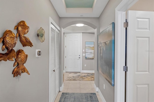 corridor featuring light tile patterned flooring, arched walkways, a raised ceiling, and baseboards