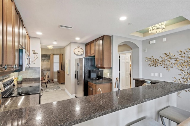 kitchen with visible vents, brown cabinets, backsplash, arched walkways, and appliances with stainless steel finishes