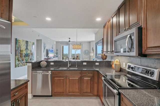 kitchen with a sink, dark stone counters, appliances with stainless steel finishes, and a peninsula