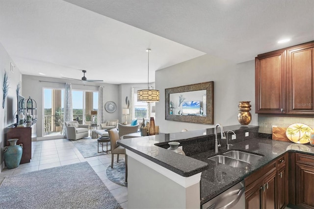 kitchen with a sink, backsplash, dark stone counters, a peninsula, and stainless steel dishwasher