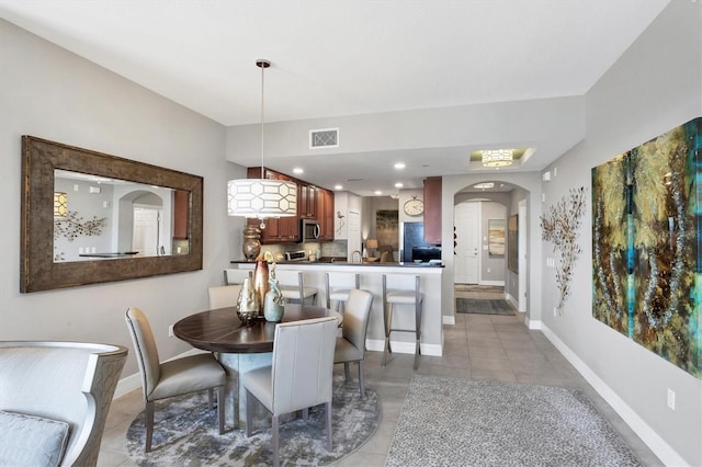 dining space with light tile patterned floors, arched walkways, visible vents, and baseboards